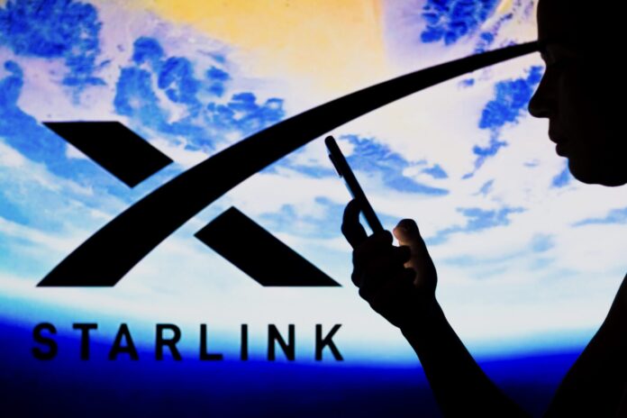 May 2, 2022, Brazil. In this photo illustration, the Starlink logo is seen in the background of a silhouetted woman holding a mobile phone.