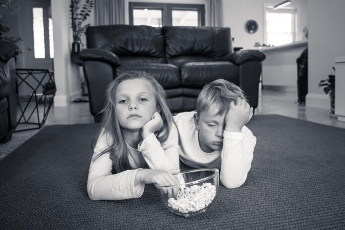 COVID-19 Outbrek. Bored brother and sister in isolation watching tv during coronavirus lockdown