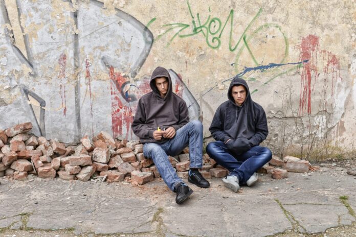 two street hooligans or rappers standing against a graffiti painted wall are preparing to smoke a cigarette